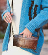 A woman wearing a blue Amina sweater holding a Bed Stu purse.