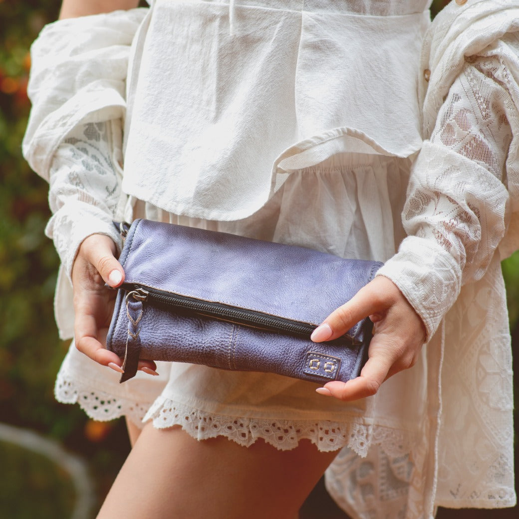 A woman in a white dress holding a Bed Stu purple clutch named Amina.