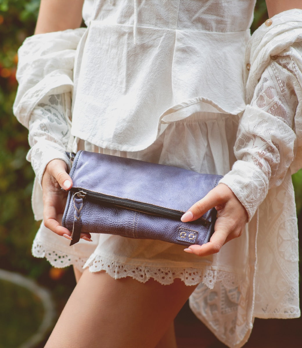 A woman in a white dress holding a Bed Stu purple clutch named Amina.