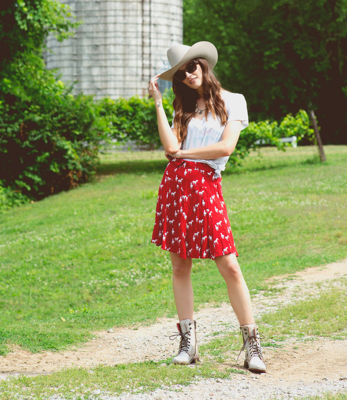 A woman wearing Bed Stu cowboy boots and a red floral skirt standing in front of a silo.