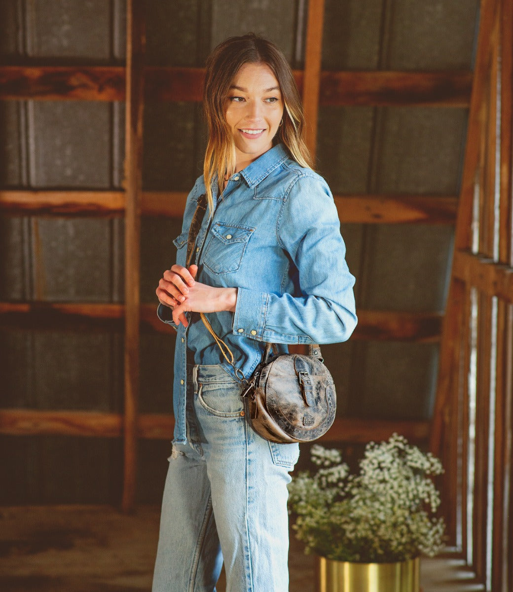 A women holding a Bed Stu Arenfield bag with a strap and buckle, made by Bed Stu.