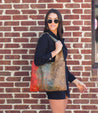 A woman wearing Bed Stu sunglasses and a black dress is standing next to a brick wall.