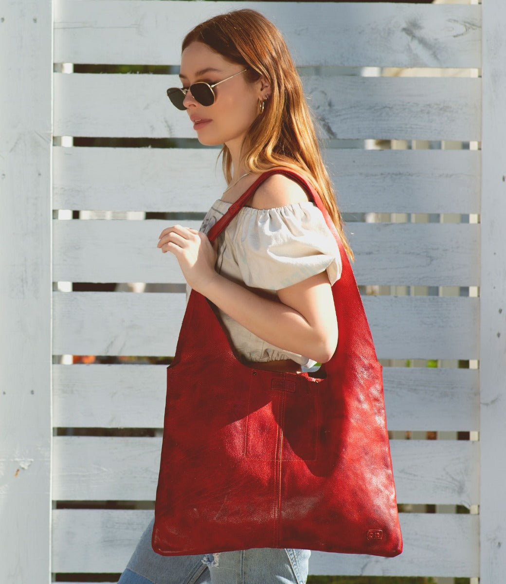 A woman carrying a red leather Ariel hobo bag by Bed Stu.