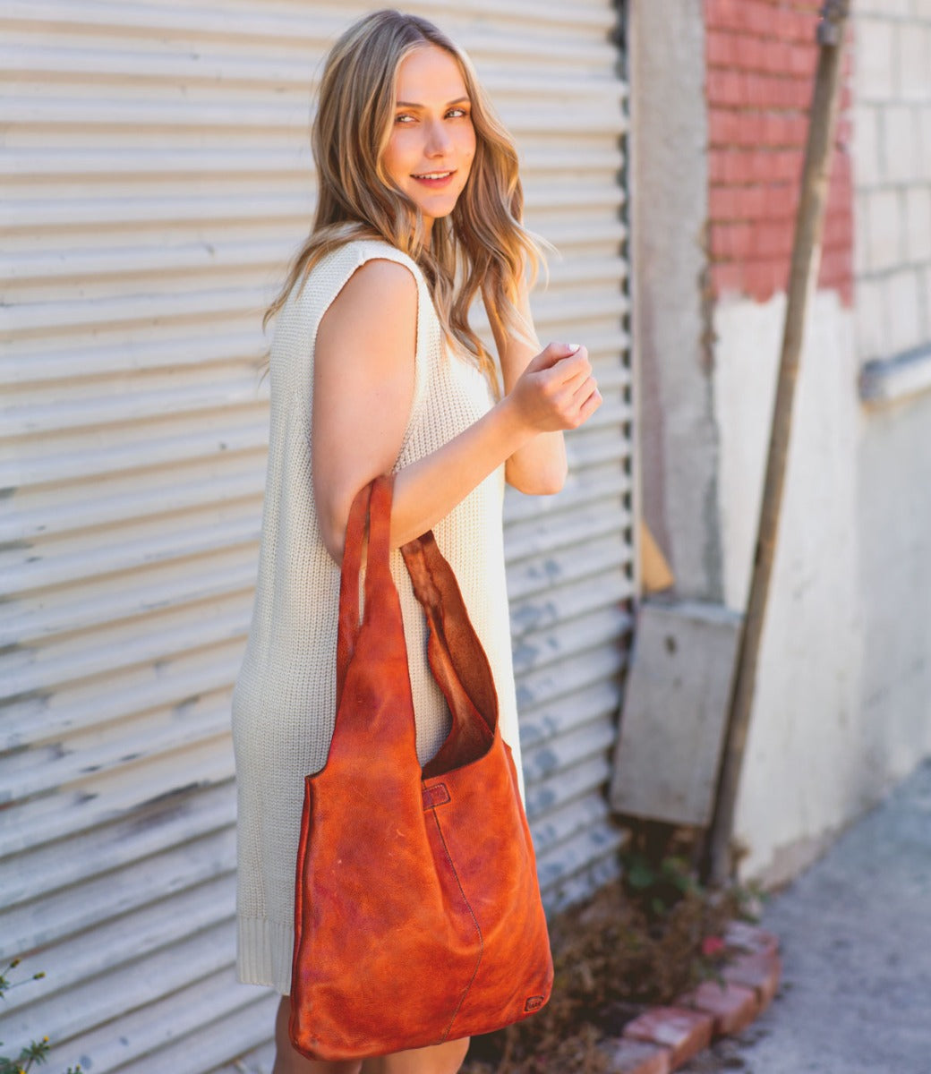 A woman in a white dress holding a Bed Stu Ariel leather bag.