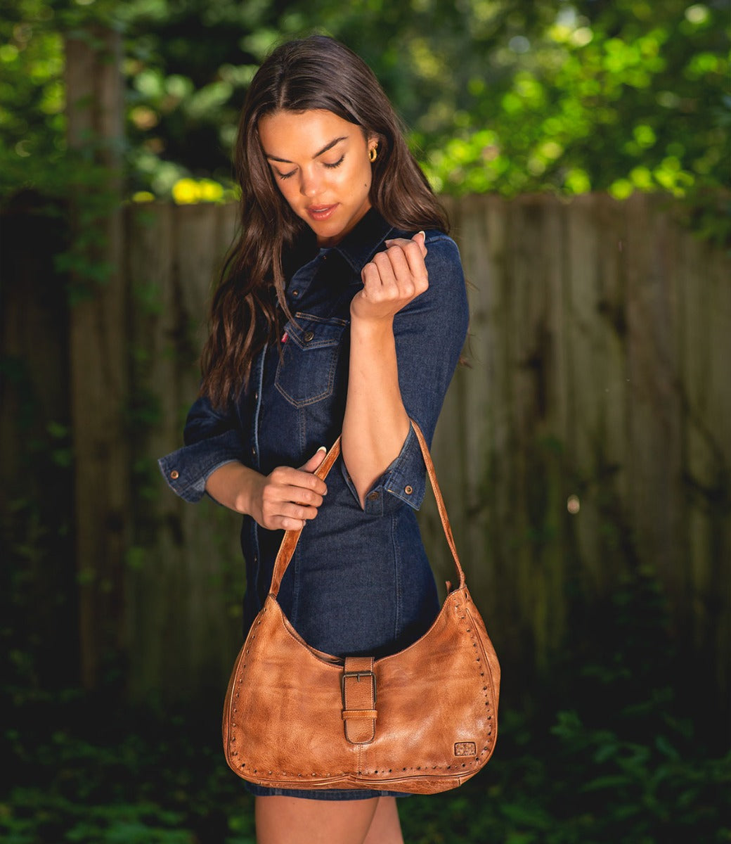 A woman wearing an Arleth denim dress holding a Bed Stu brown leather purse.