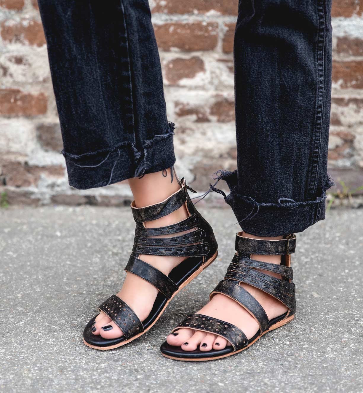 A woman wearing black Artemis gladiator sandals and jeans by Bed Stu.