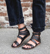 A woman wearing black Artemis gladiator sandals and jeans by Bed Stu.