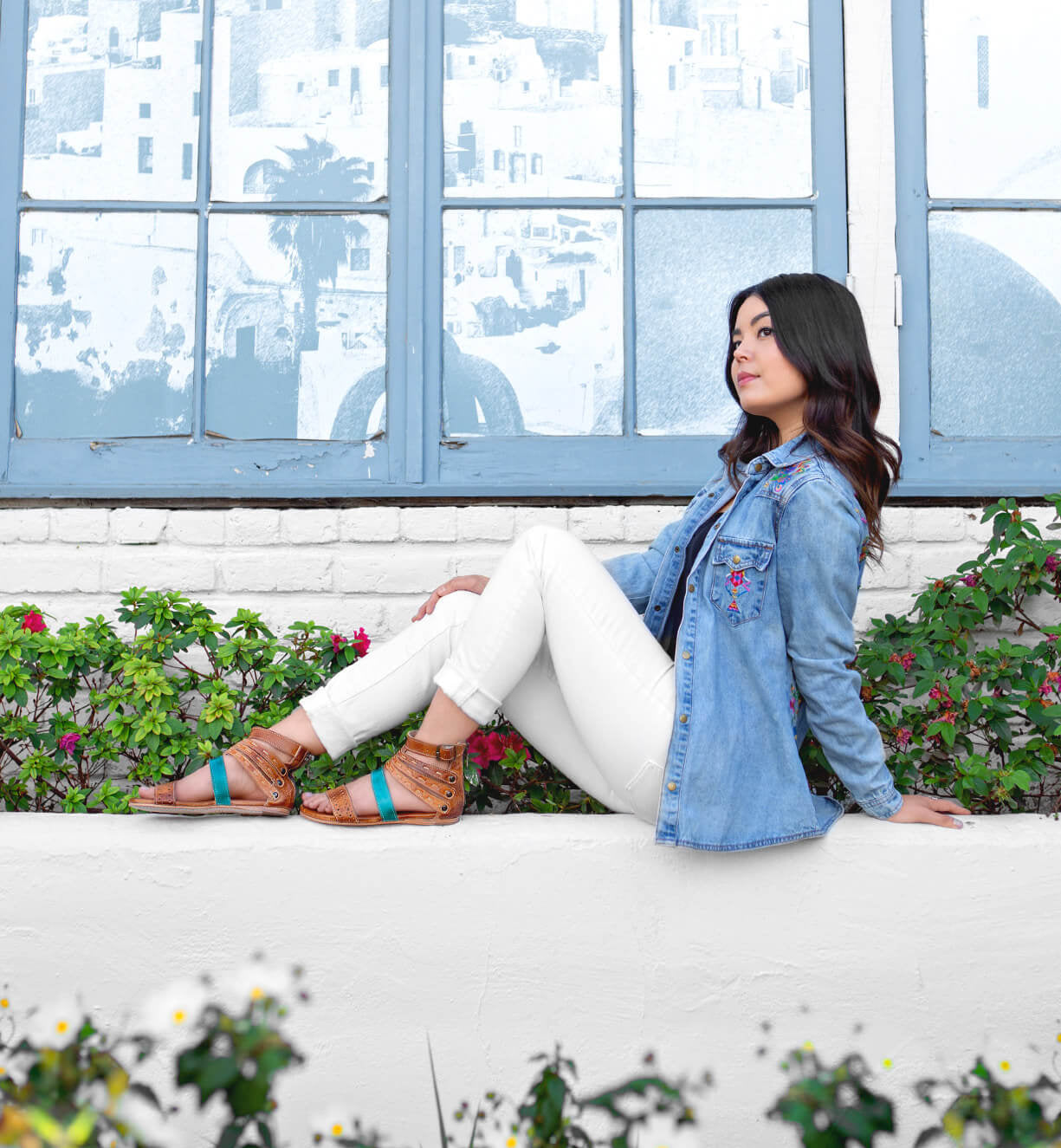 A woman sitting on a ledge with flowers and an Artemis denim jacket from Bed Stu.