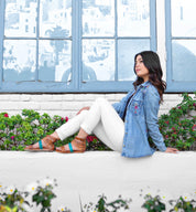 A woman sitting on a ledge with flowers and an Artemis denim jacket from Bed Stu.