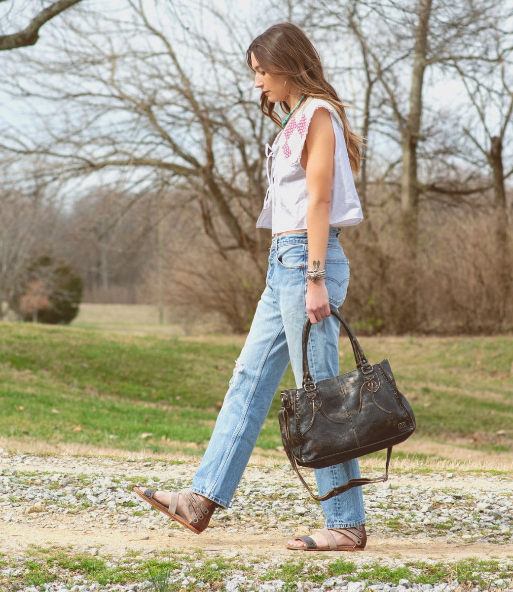 A woman wearing jeans and an Artemis purse walking down a dirt road by Bed Stu.