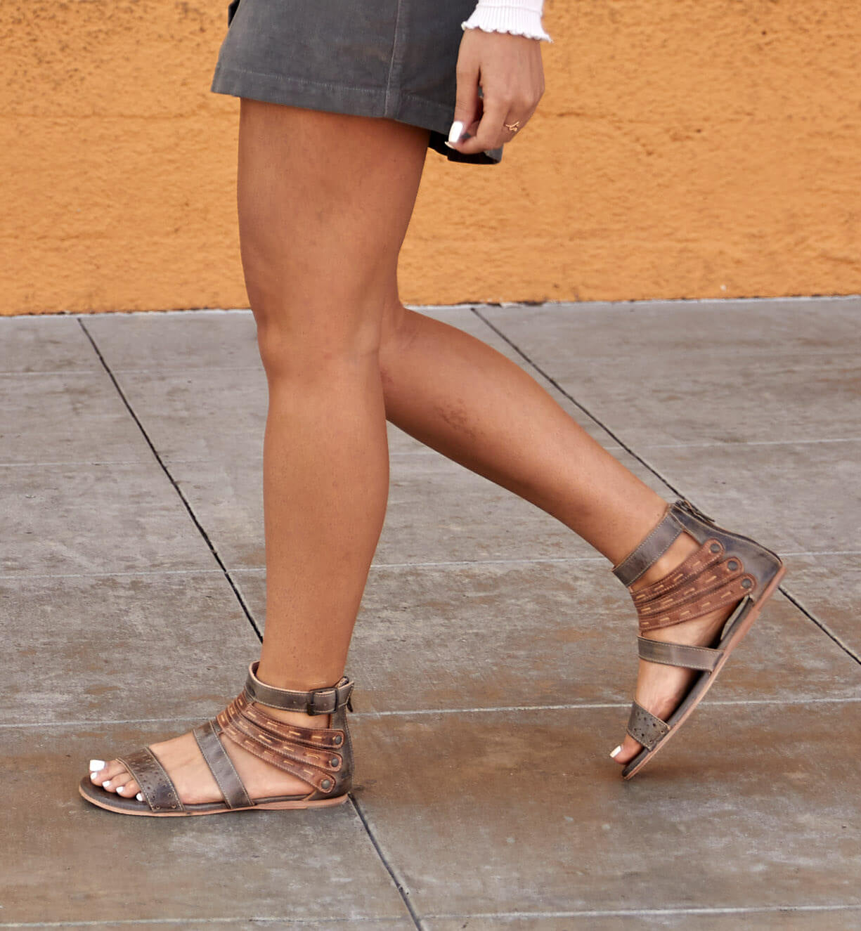 A woman wearing a gray skirt and Bed Stu sandals.