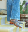 A woman wearing a pair of blue jeans and a pair of gray Asenet Bed Stu loafers.