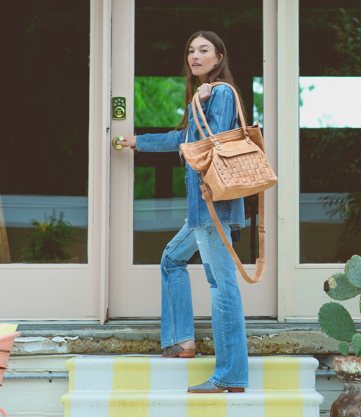 A woman is standing on the steps of a house holding a Bed Stu Asenet bag.