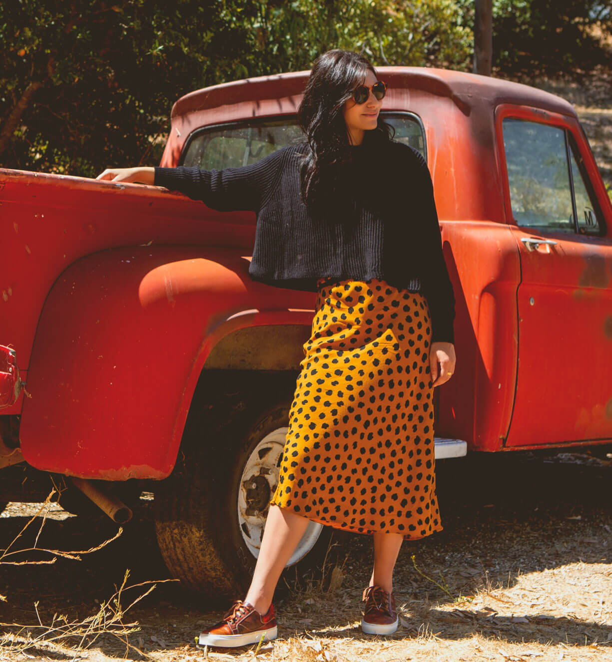 A woman leaning against a Bed Stu Azeli truck in a polka dot skirt.