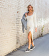 A woman in a white Azeli dress walking down a brick wall. Brand: Bed Stu.