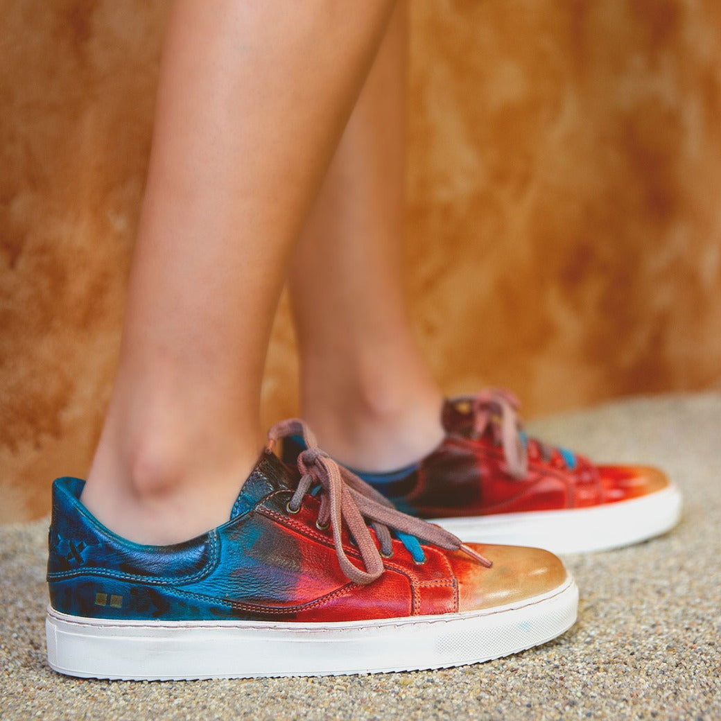 A woman wearing a pair of Bed Stu Azeli sneakers with colorful paint on them.