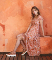 A woman in an Azeli dress by Bed Stu is posing on an orange wall.