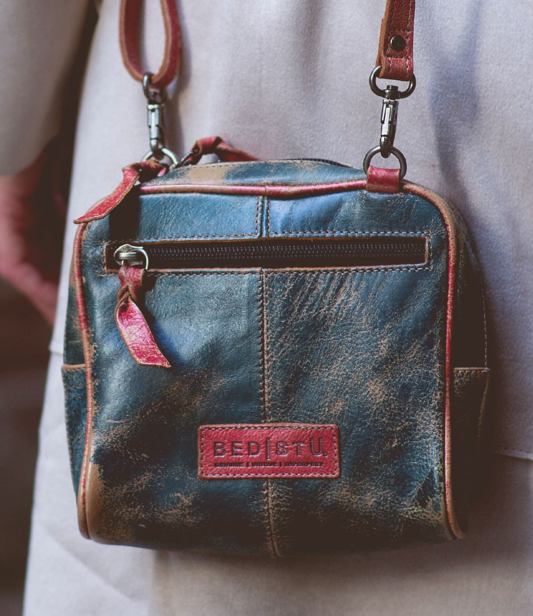 A woman is holding a blue and red Capture cross body bag from Bed Stu.