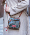A woman wearing a trench coat holding a Bed Stu Capture cross body bag.
