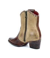 The Baila II by Bed Stu is a brown and beige ankle boot featuring a side zipper, a wooden heel, and a pointed toe that enhances its western-inspired charm.