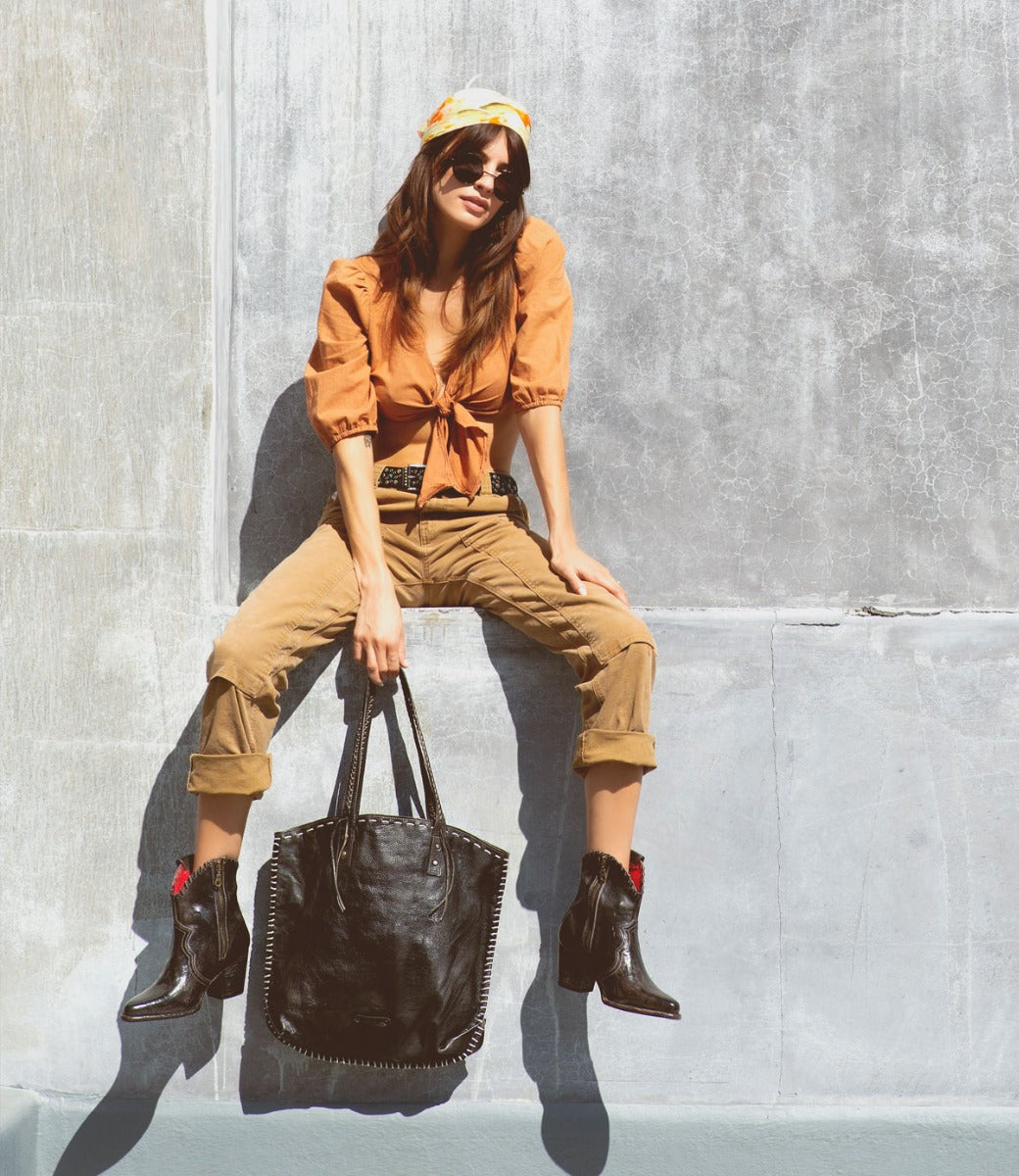 A woman sitting on a wall holding a Bed Stu Barra bag.