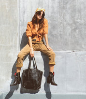 A woman sitting on a wall holding a Bed Stu Barra bag.
