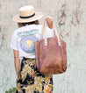 A woman wearing a hat and floral skirt carrying a Bed Stu Barra tote bag.