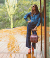 A woman is standing on a wooden deck holding a Bathsheba bag by Bed Stu.