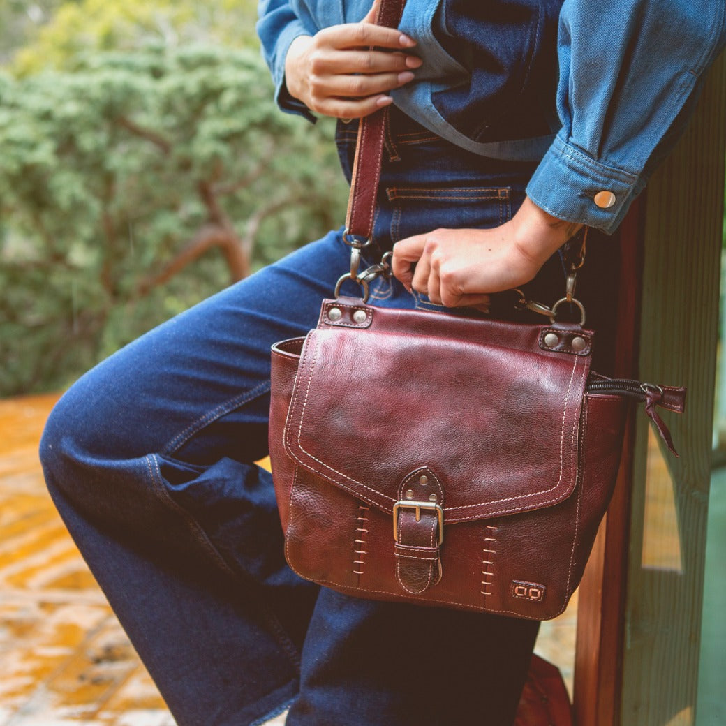 A woman is holding a Bed Stu Bathsheba burgundy leather bag.