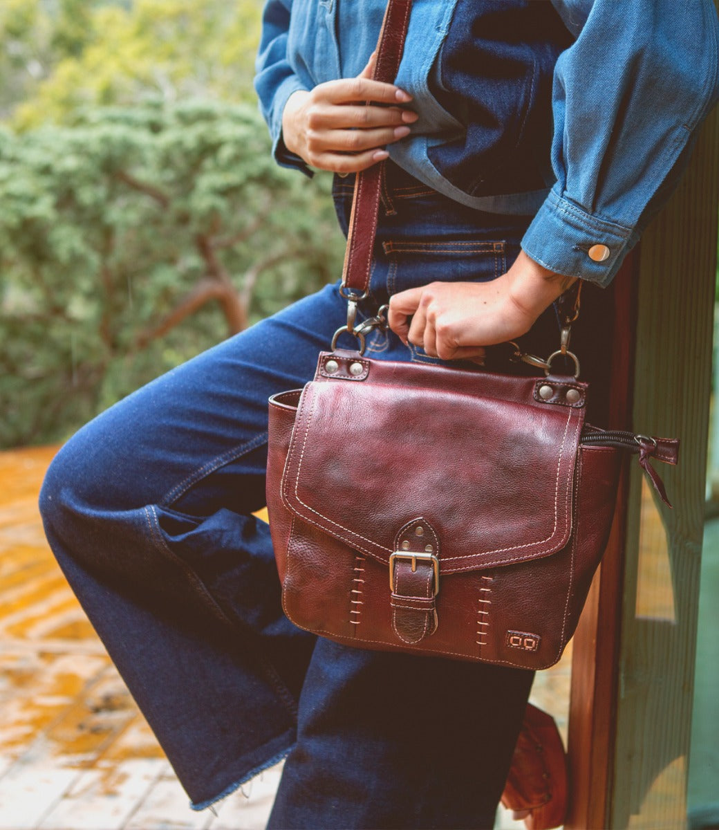 A woman is holding a Bed Stu Bathsheba burgundy leather bag.