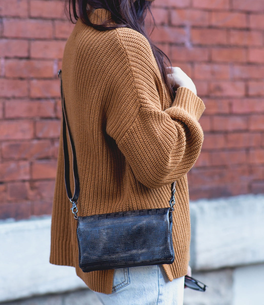 A woman wearing a tan sweater and jeans holding a Bed Stu Bayshore crossbody bag.