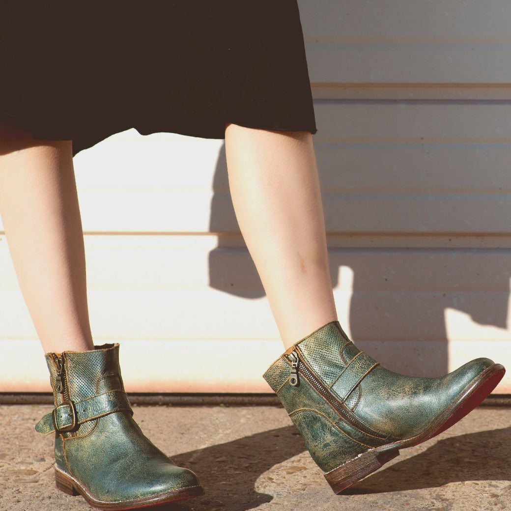 A woman wearing a pair of Bed Stu Becca teal leather boots.