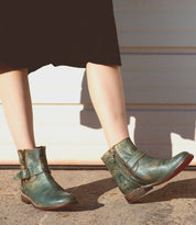 A woman wearing a pair of Bed Stu Becca teal leather boots.