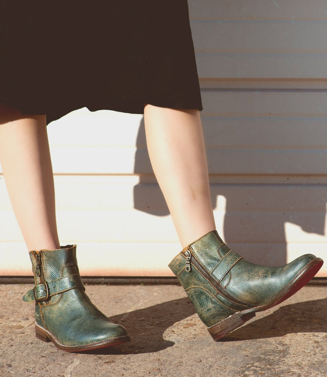 A woman wearing a pair of Bed Stu Becca teal leather boots.