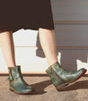 A woman wearing a pair of Bed Stu Becca teal leather boots.