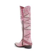The "Betting" boot by Bed Stu is a pink leather knee-high Western boot with cutout floral designs, stud detailing, a decorative harness strap, and a convenient side zipper.