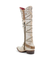 The "Betting" boot by Bed Stu is a tall beige Western style, crafted from vegetable-tanned leather, embellished with decorative studs and floral embroidery. It features a side zipper and low heel.