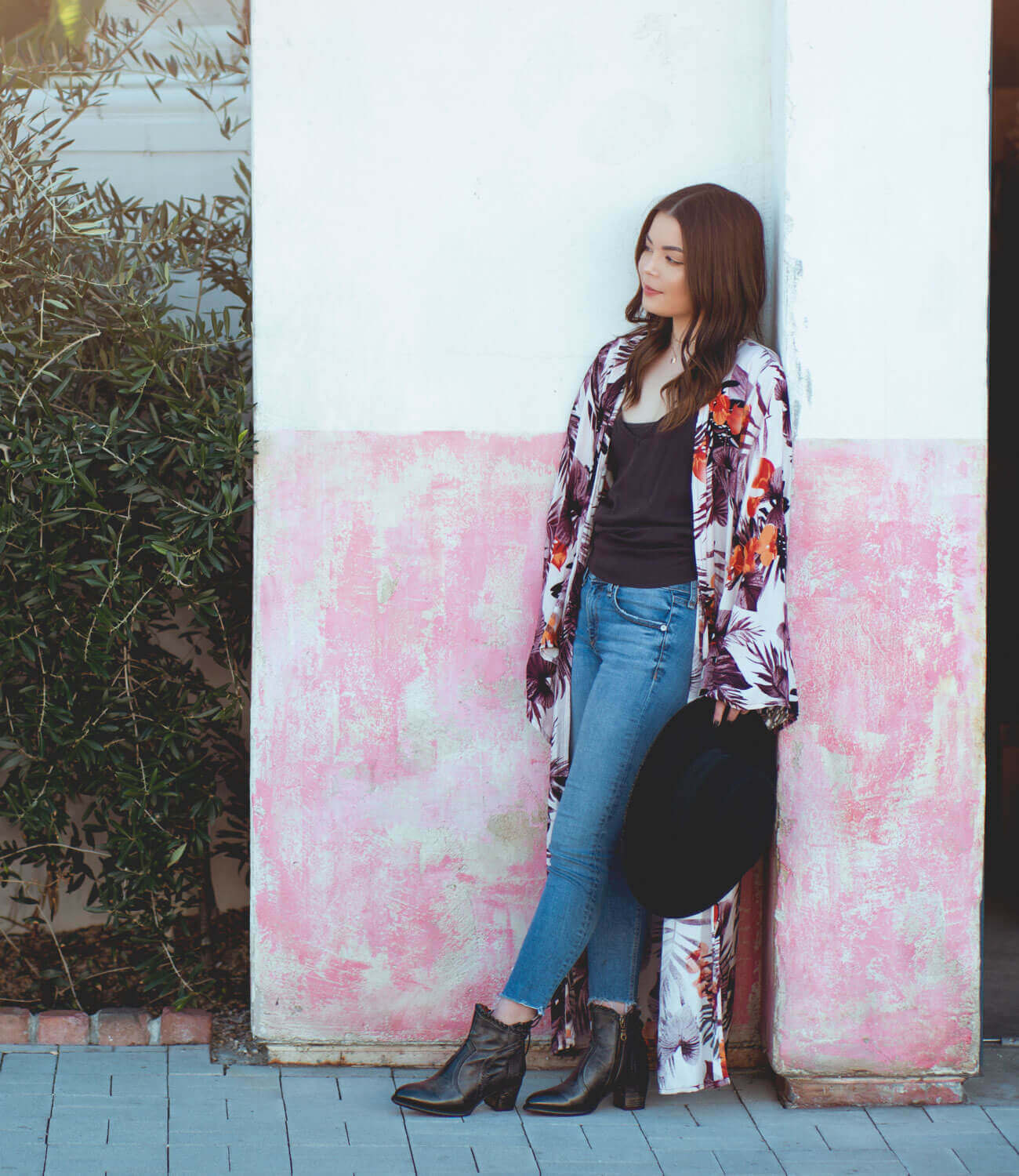 A woman is leaning against a wall wearing a Bed Stu floral kimono.