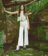 A woman standing in the woods wearing Bed Stu Bia white pants and boots.