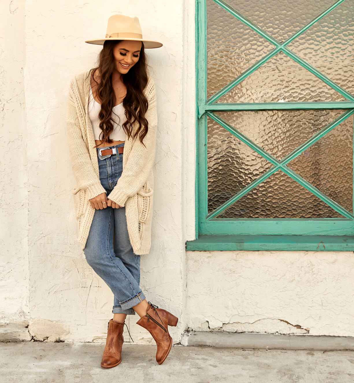 A woman in Bed Stu jeans and a Bed Stu hat leaning against a wall.