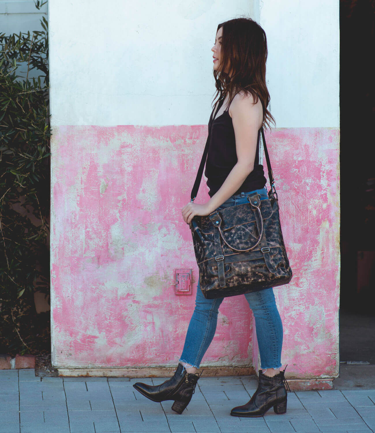 A woman is walking with a Bed Stu Big Fork tote bag in front of a pink wall.