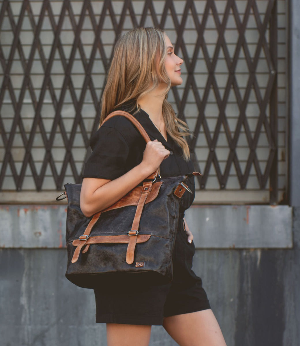 A woman wearing black shorts and a black Bed Stu Big Fork leather bag.