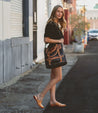 A woman is walking down the street holding a Big Fork bag by Bed Stu.