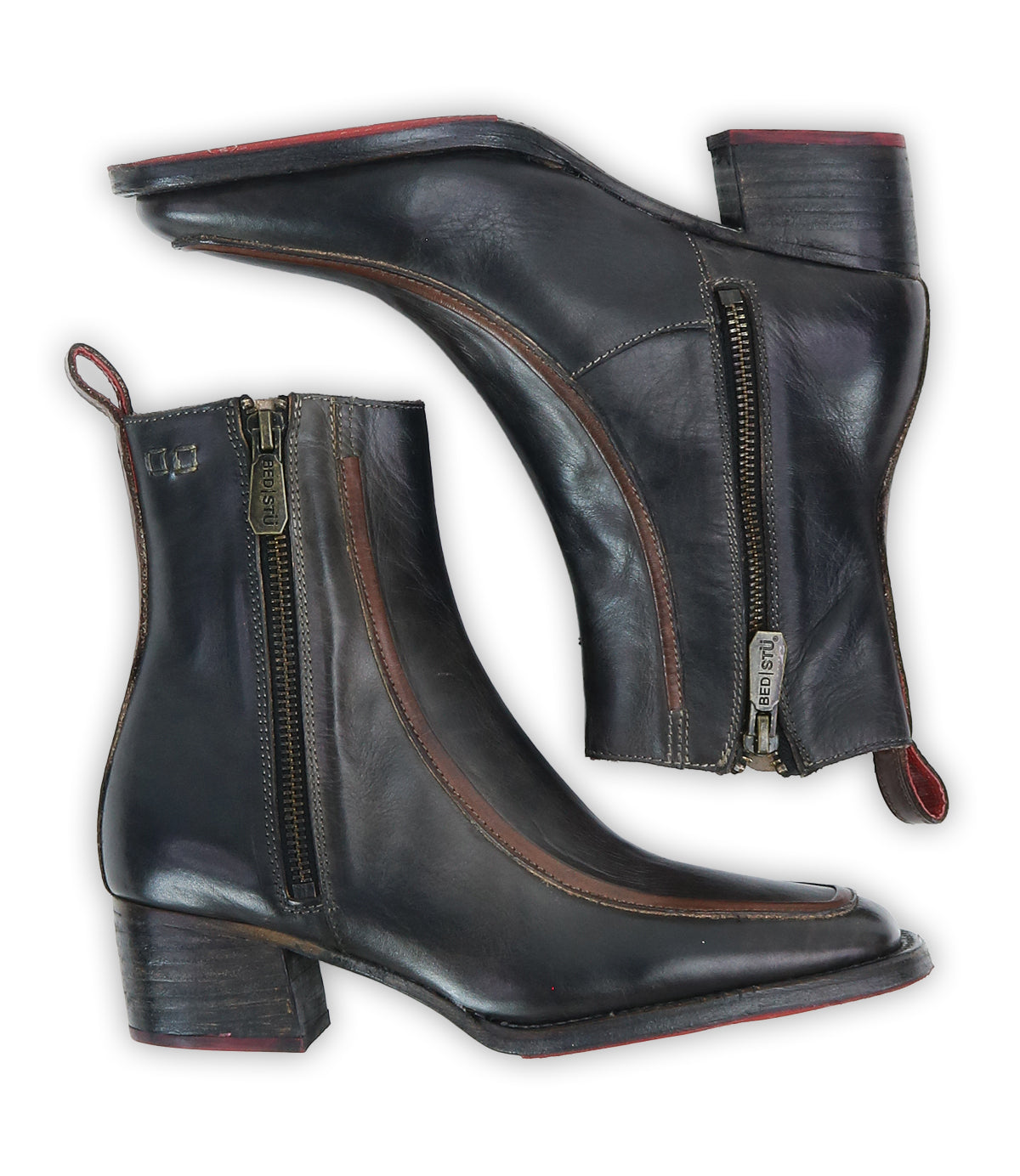 The Bed Stu Bitsy is a pair of black hand-finished leather ankle boots featuring side zippers, brown trim accents, stacked wooden heels, and red pull tabs, shown on a white background.