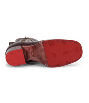 The Bed Stu Bitsy is a brown leather ankle boot shown from the bottom, with a worn red sole, visible stitching, subtle patterns, and a stacked wooden heel made from hand-finished leather.