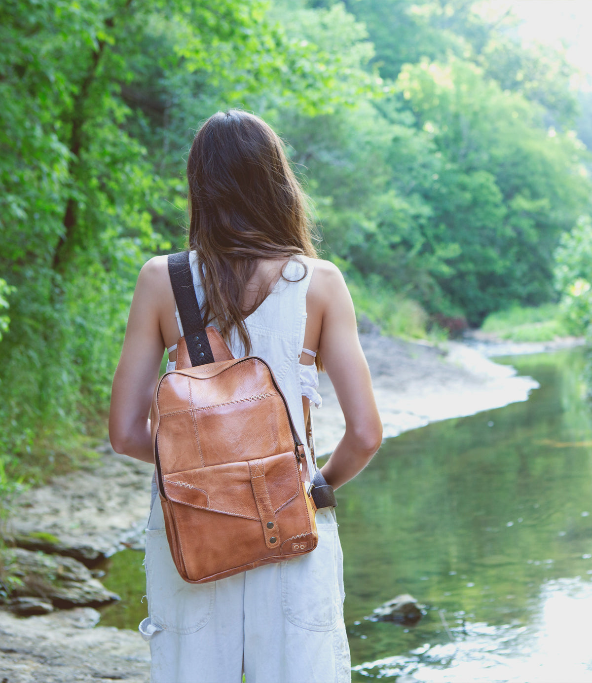 A woman standing by a river with a Bed Stu Boss bag.