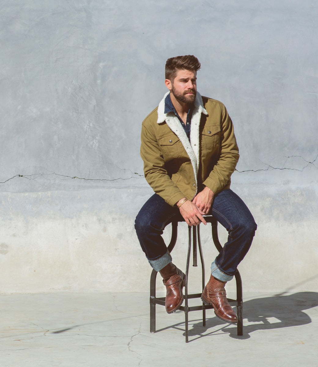 A man sitting on a stool wearing a Bed Stu Brando jacket and jeans.