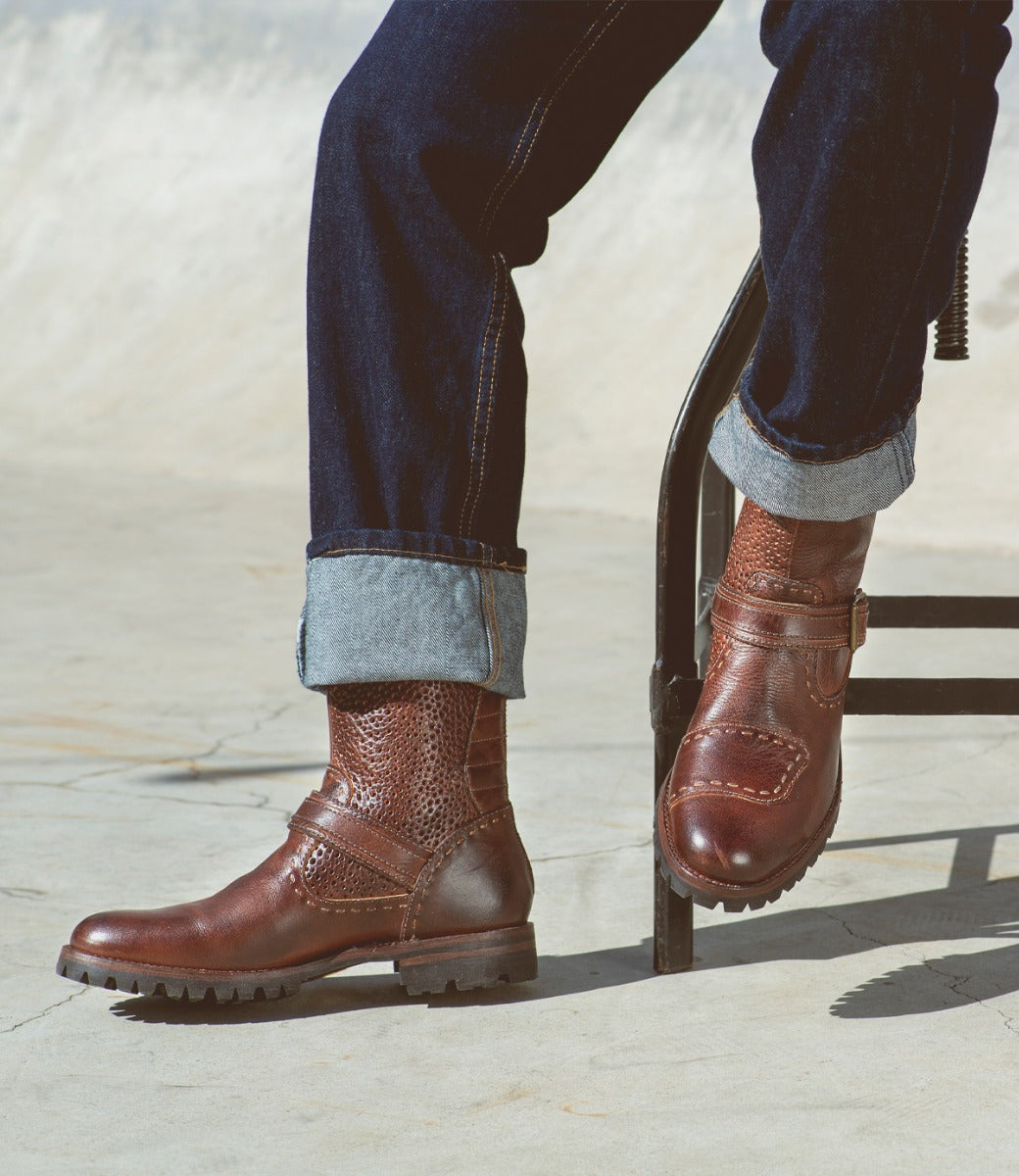 A man sitting on a chair wearing brown Bed Stu Brando leather boots.