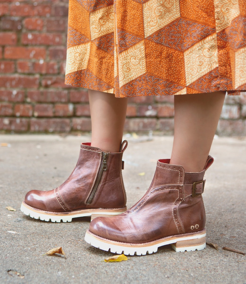 A woman wearing Brianna boots by Bed Stu and an orange skirt.