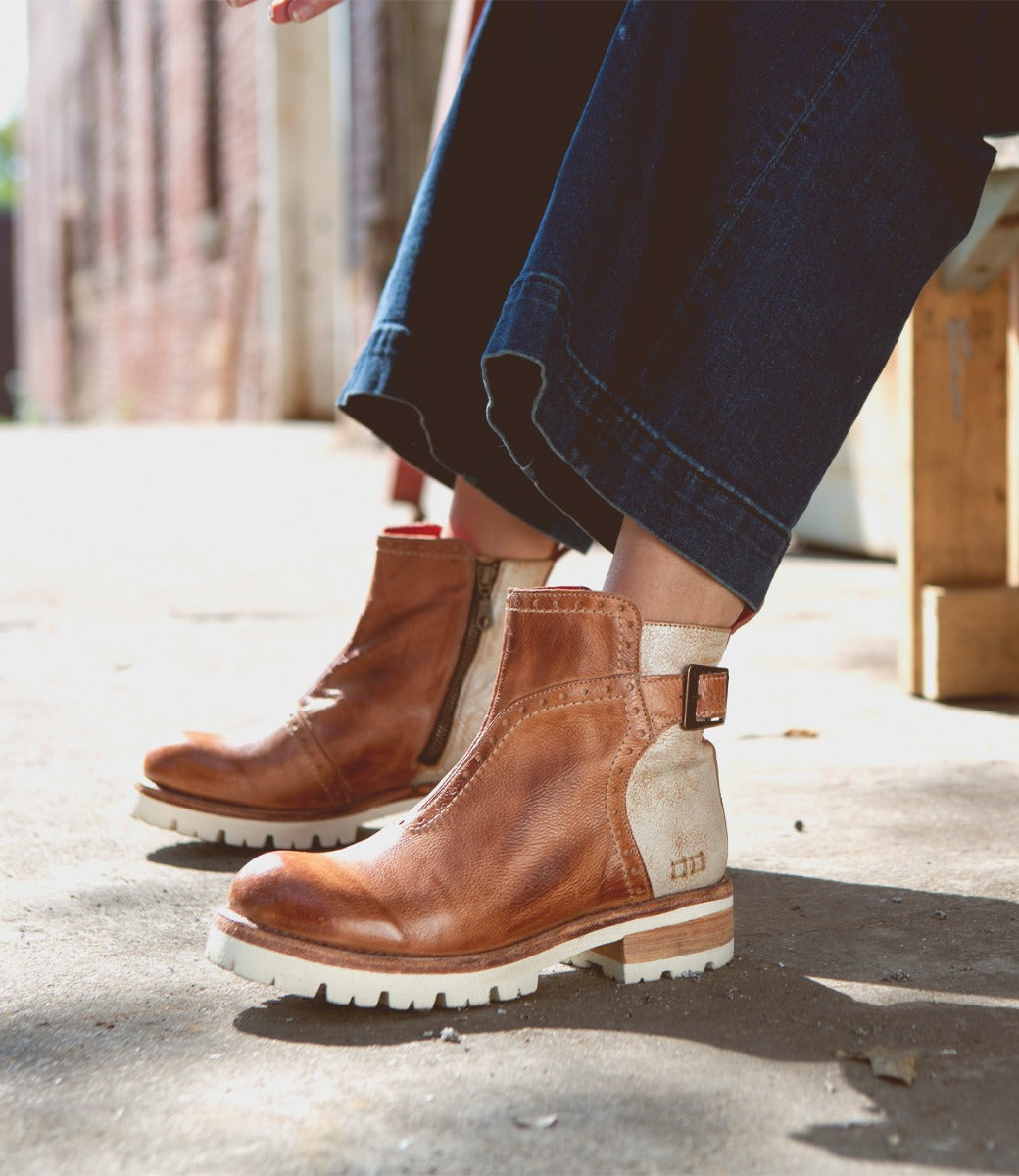 A woman is sitting on a bench wearing a pair of Bed Stu Brianna brown boots.